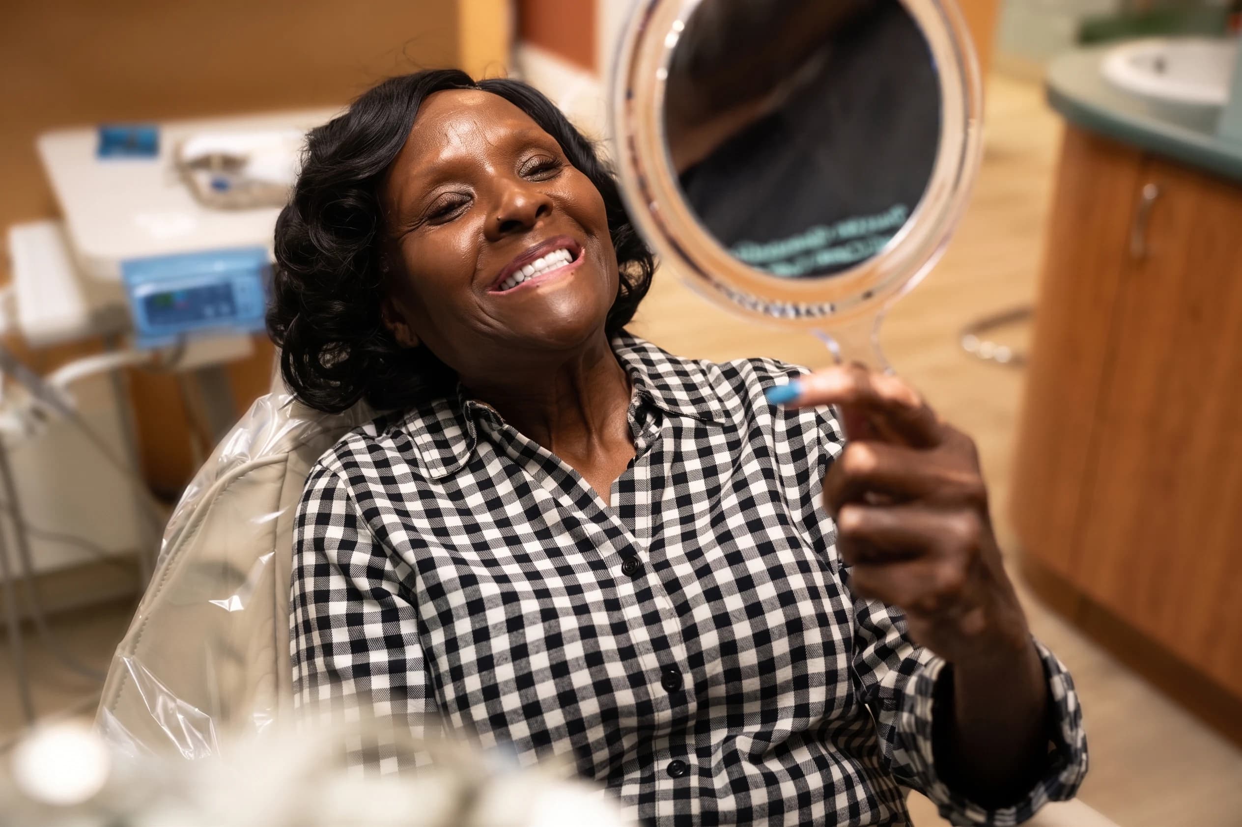 A patient beaming as she checks her smile in a hand mirror