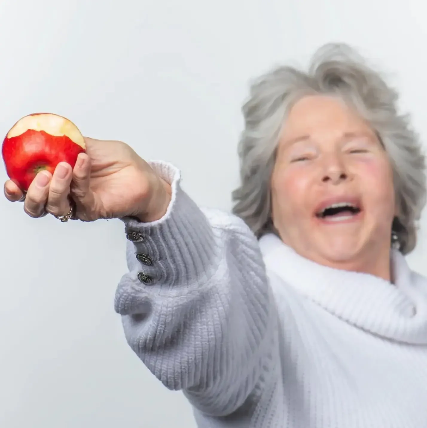 A patient laughing as she holds up an apple after treatment