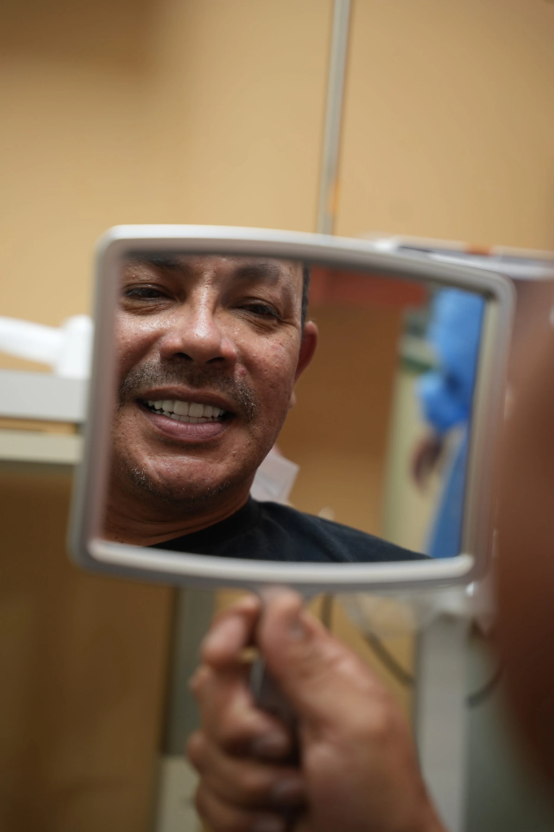 A patient smiling at his reflection in a hand mirror