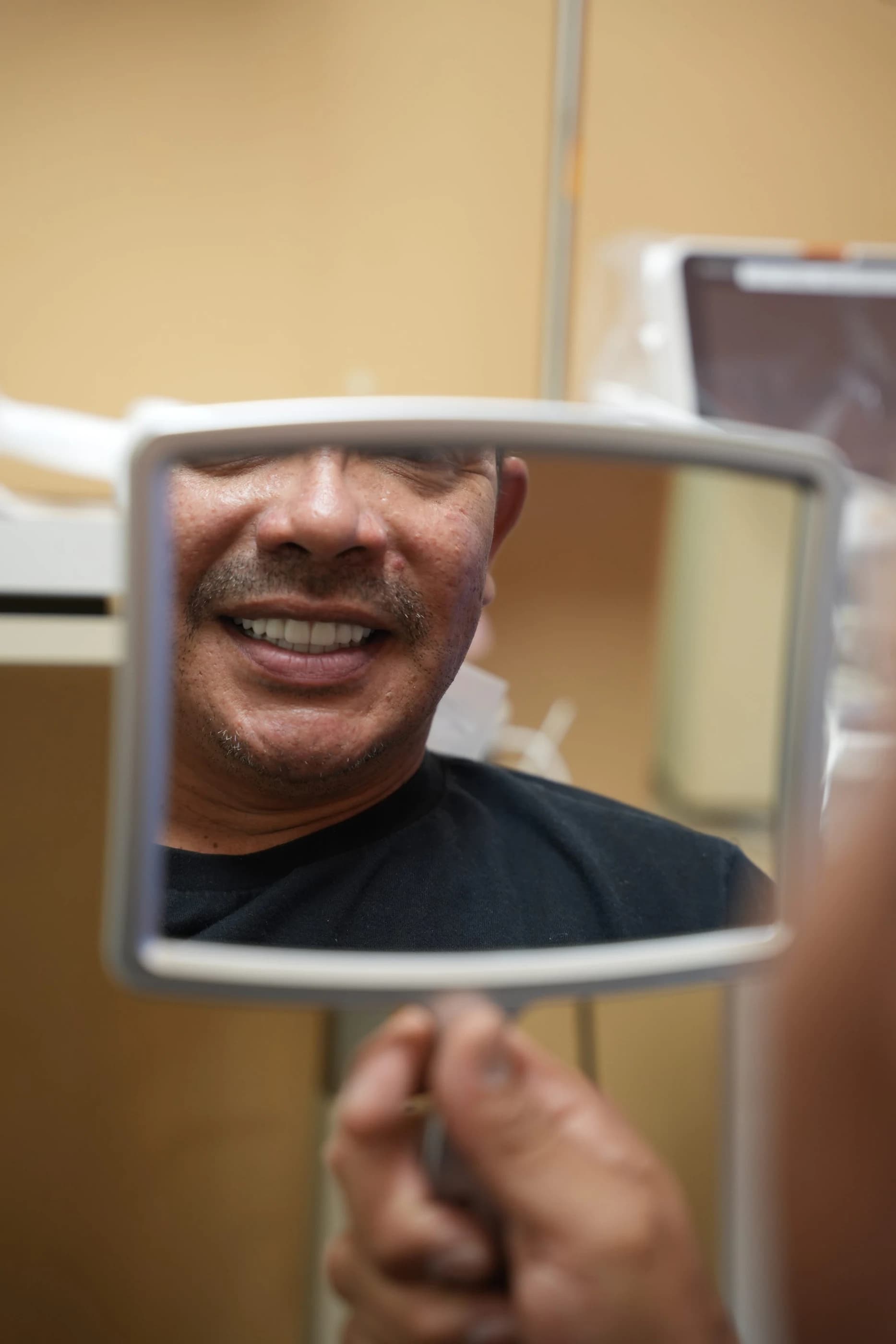 Un paciente sonriendo mientras sostiene un espejo de mano en la sala de tratamiento