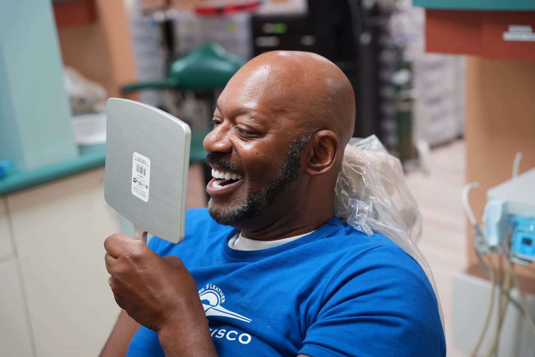 Un paciente riéndose de su nueva sonrisa en un espejo de mano