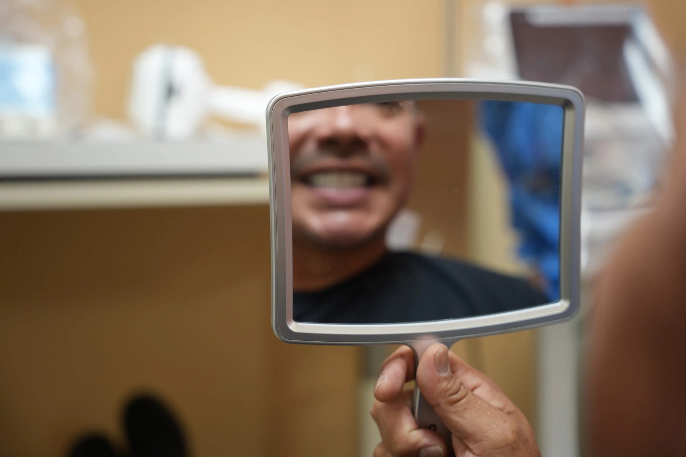 A patient smiling at his reflection in a hand mirror