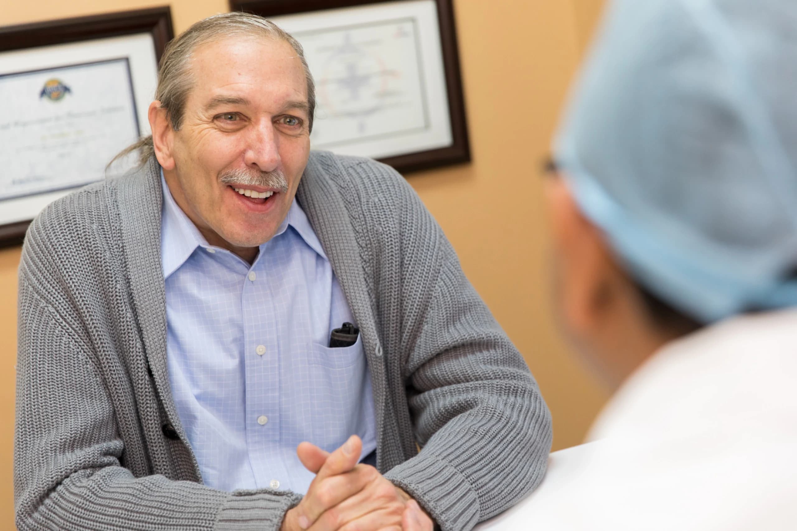Un paciente con suéter gris conversando con un doctor vestido con ropa quirúrgica