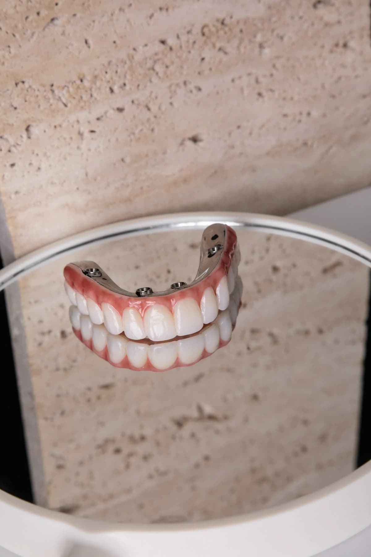 Prótesis de arcada completa de zirconia terminada, reflejada sobre una superficie oscura